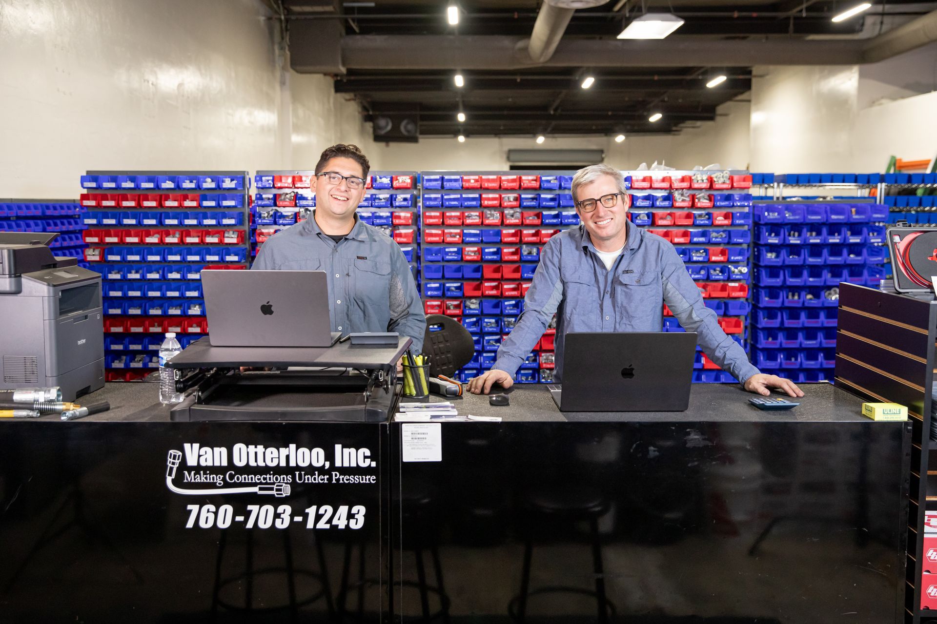 Two men are sitting at a desk with the Van Otterloo, Inc. logo laptops in a store.