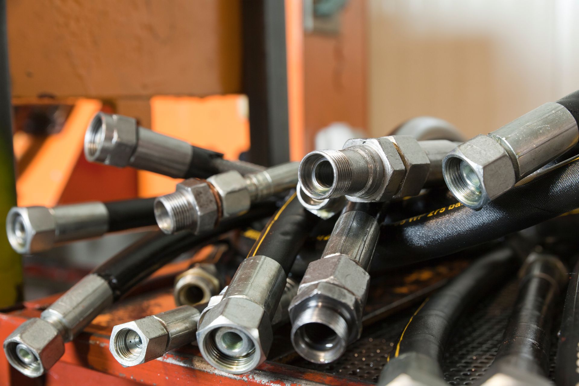 Hydraulic hoses with metal fittings, piled on a red surface.
