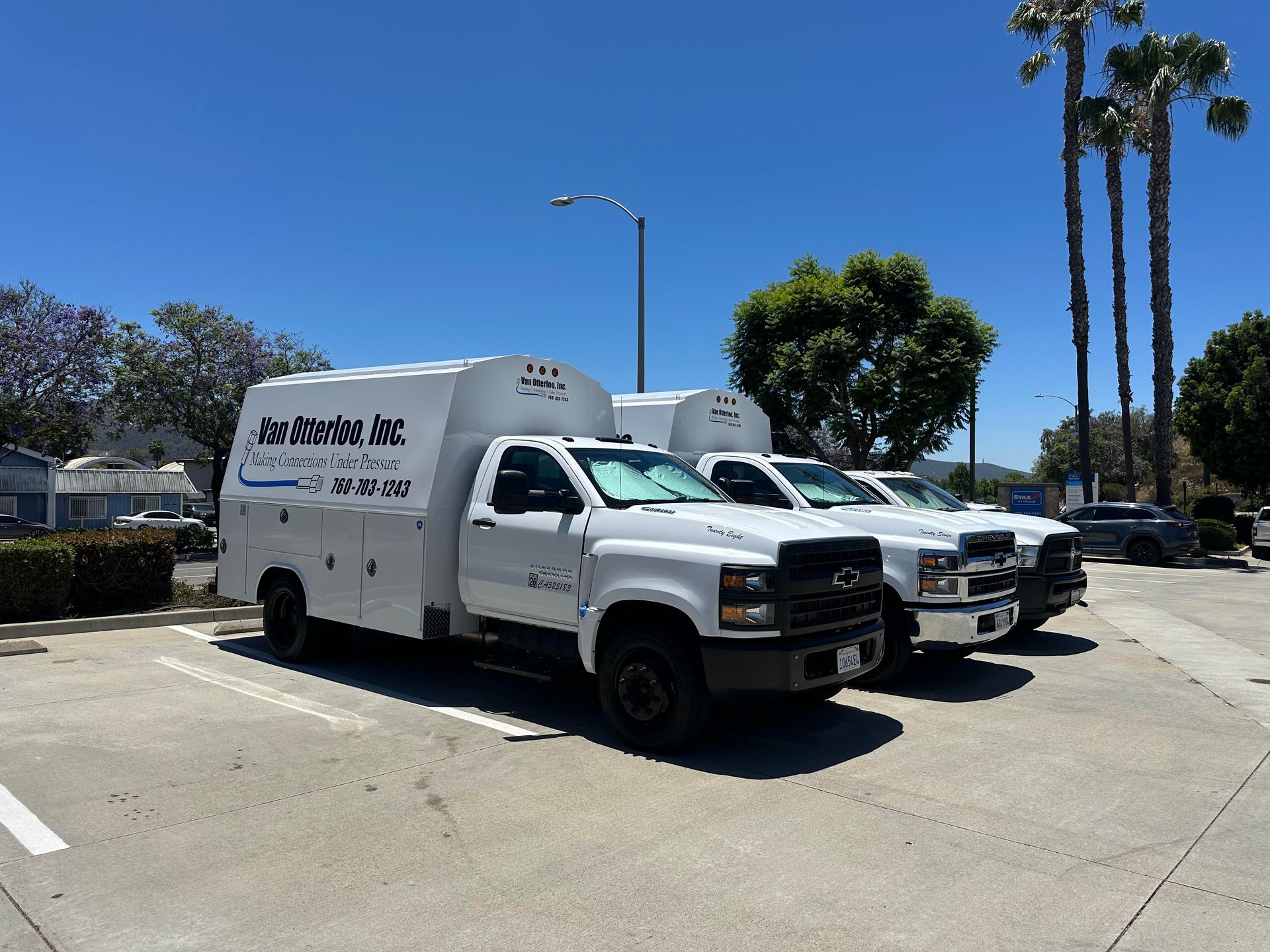 Three white service trucks parked in a lot under a blue sky, some palm trees.