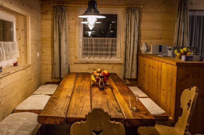 Ein rustikaler Essbereich in einer Holzhütte mit einem langen Holztisch, einer Sitzbank mit Kissen und warmen Pendelleuchten.