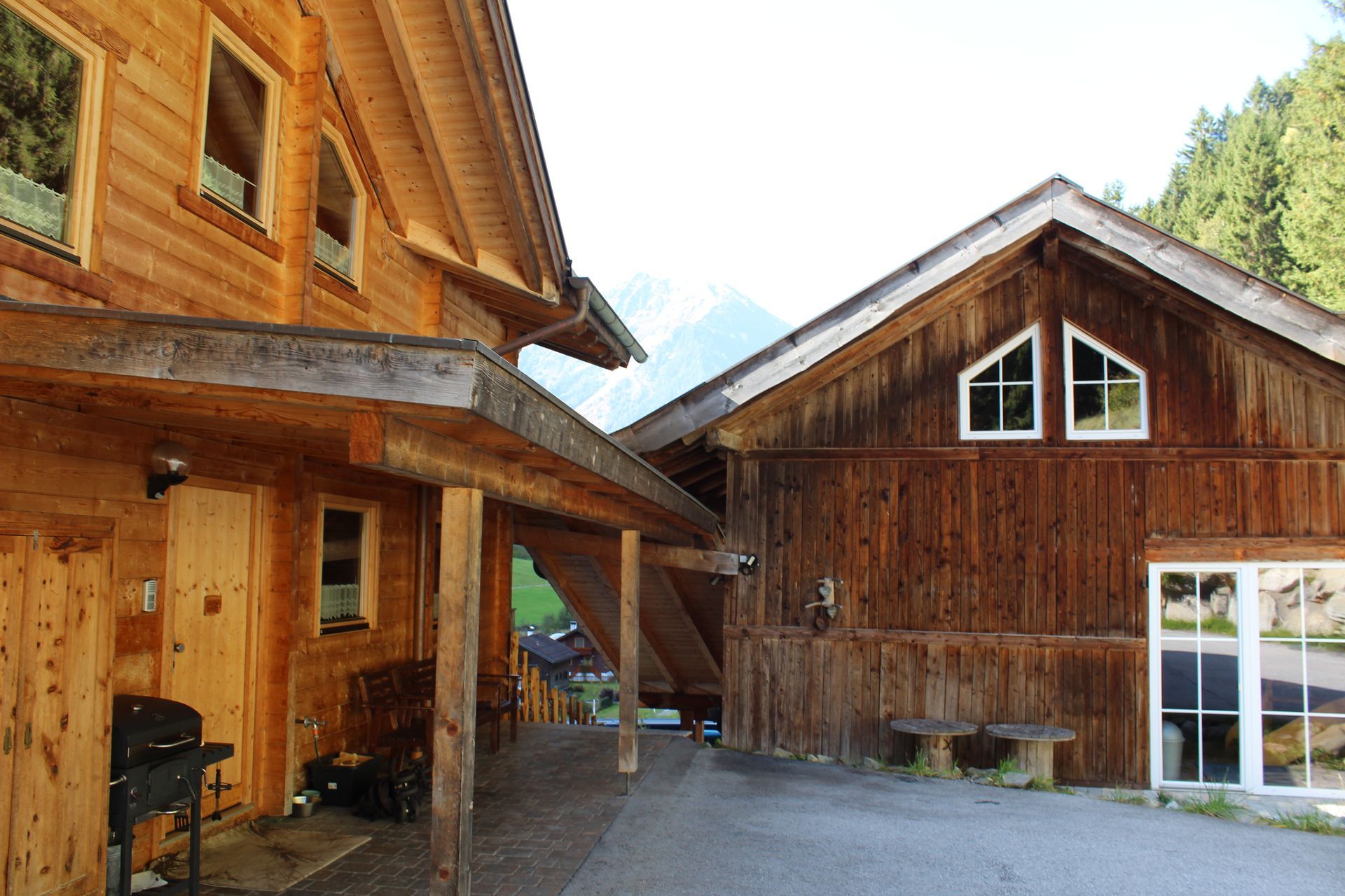 Zwei rustikale Holzgebäude mit Giebeldächern in alpiner Umgebung mit einem Kieshof.