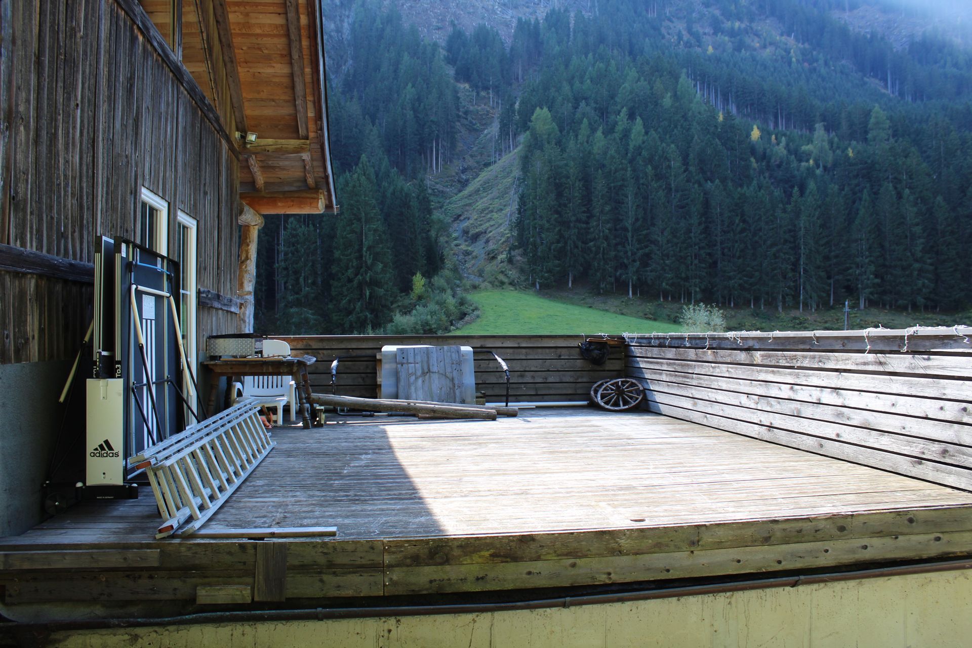 Der Balkon einer hölzernen Berghütte mit Leiter und Baumaterialien bildet einen Kontrast zum Nadelwald.