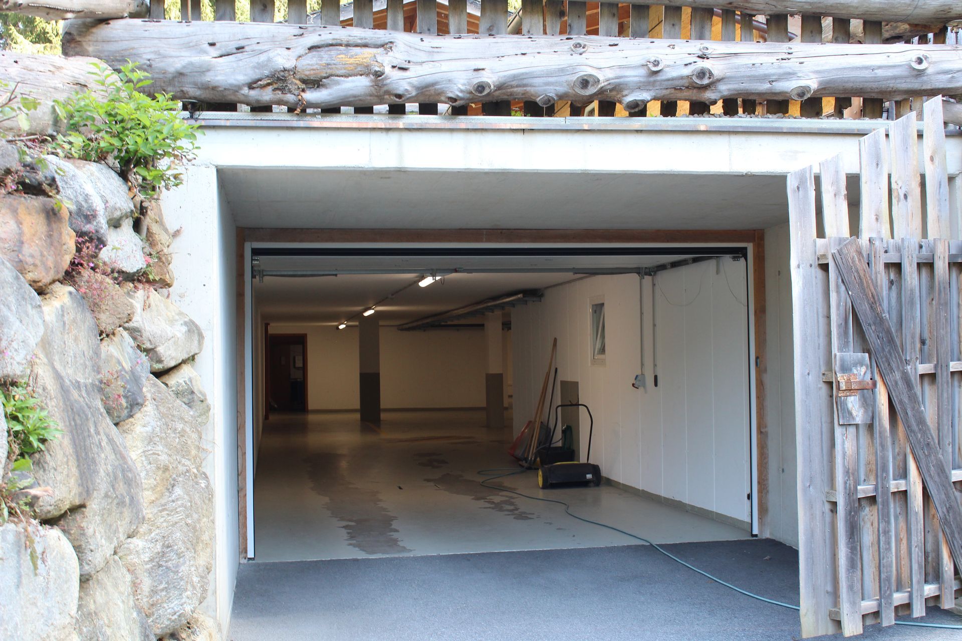 Offene Tiefgarage mit weißen Wänden, grauem Boden und einer über dem Eingang errichteten Holzzaunkonstruktion.
