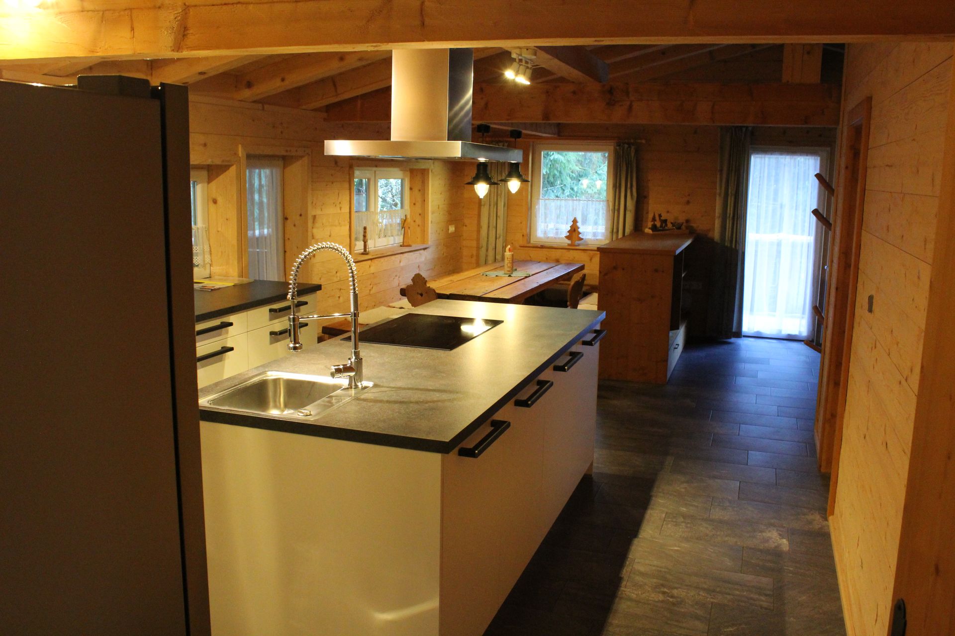 Ein rustikaler, offener Wohnbereich mit einer modernen Kücheninsel mit Spüle, holzgetäfelten Wänden und einem Essbereich.