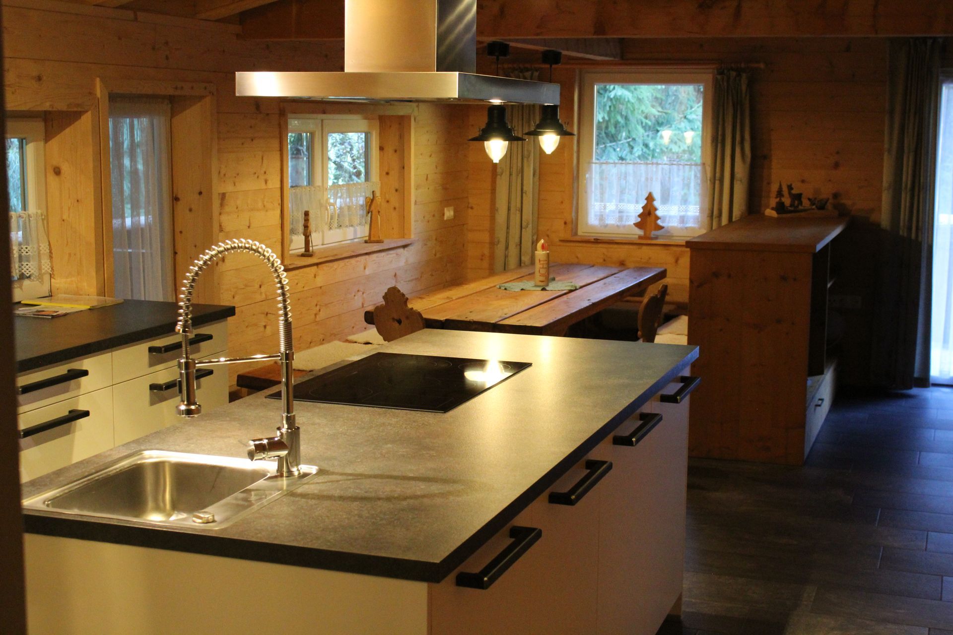 Eine rustikale Küche mit Holzinterieur, einer Kochinsel mit Spüle und Kochfeld sowie einem hölzernen Esstisch im Hintergrund.