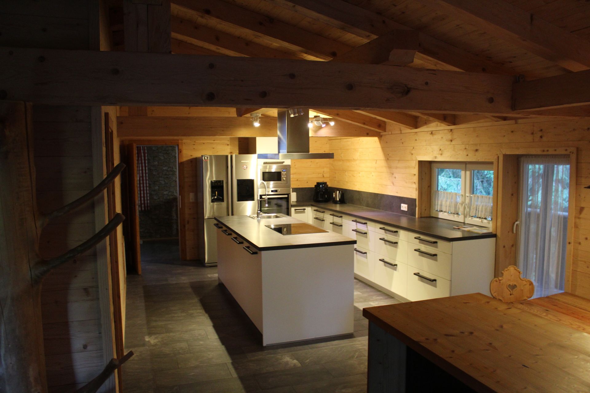 Moderne Küche mit weißer Kochinsel, Edelstahlgeräten und Holzwänden in einer rustikalen, offenen Hütte.