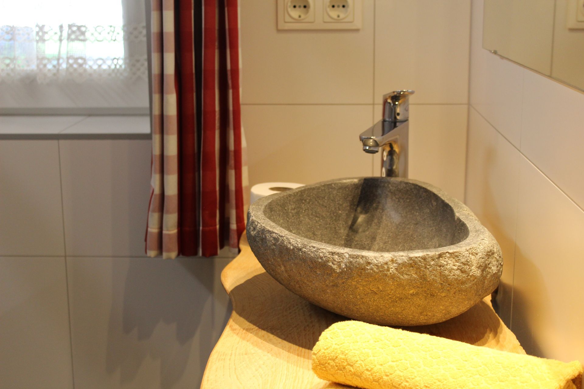Auf einer Holztheke steht ein Steinwaschbecken mit einem gelben Handtuch daneben