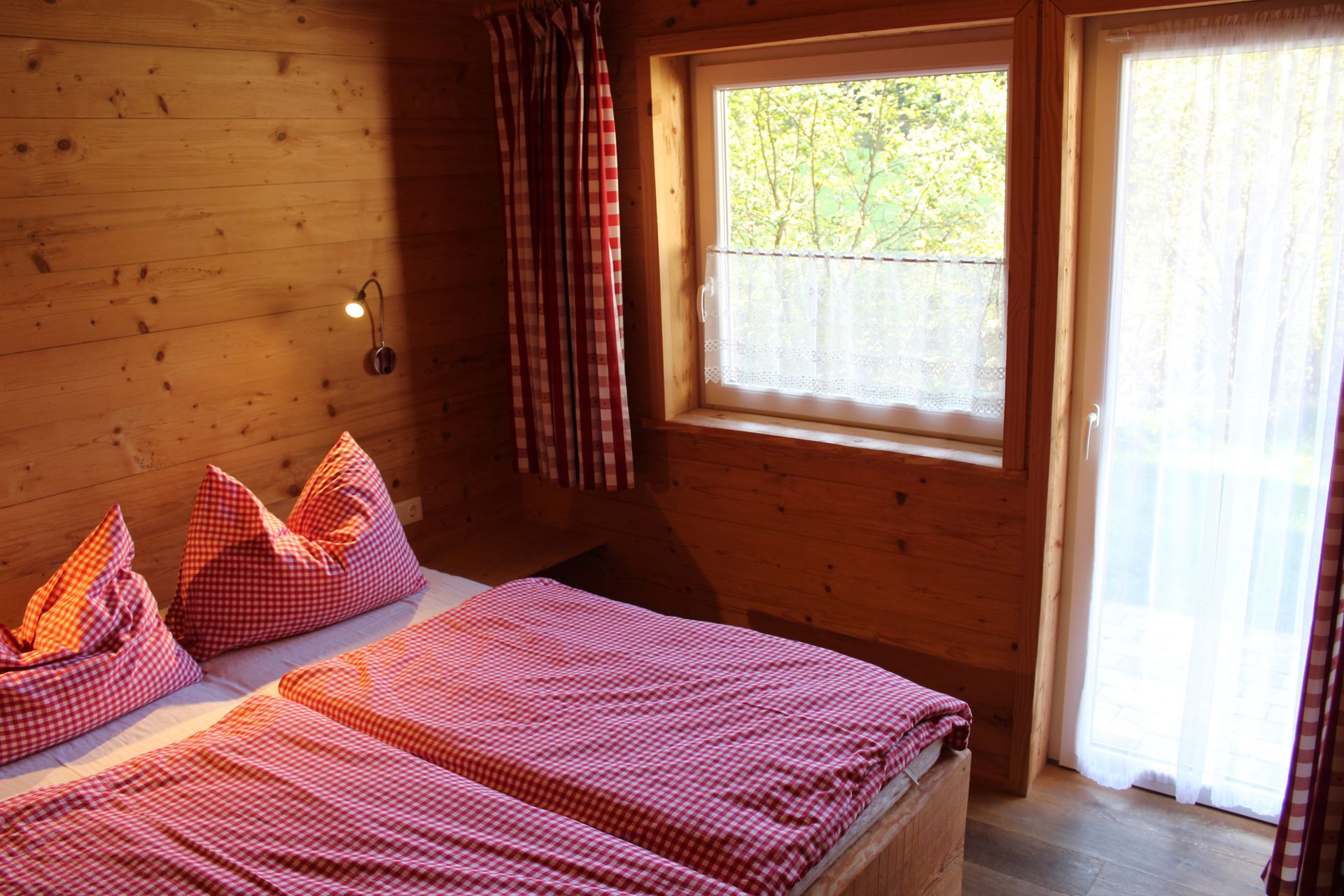 Ein gemütliches Schlafzimmer mit Holzwänden, einem Bett mit rot-weiß karierter Bettwäsche