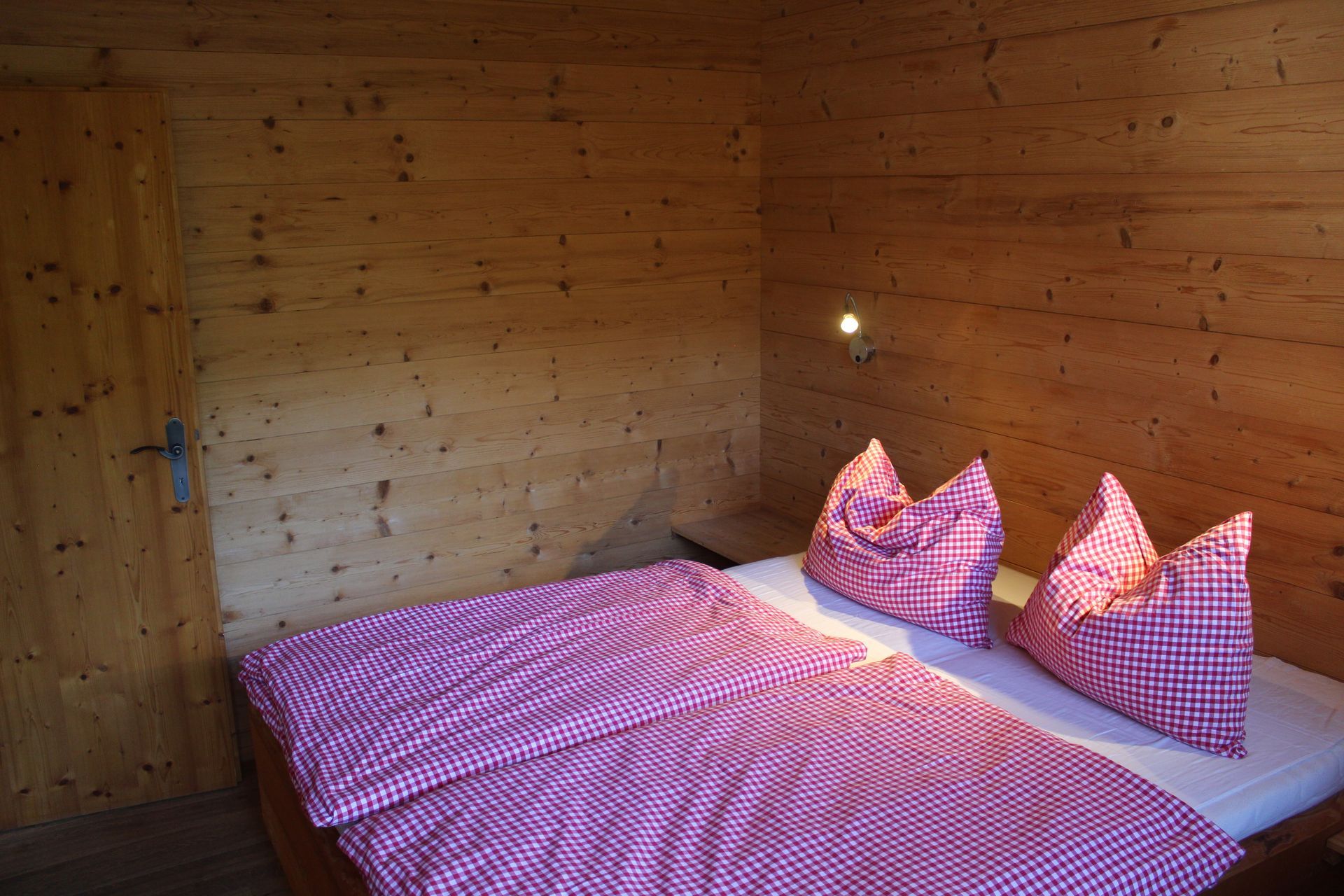 Ein rustikales Schlafzimmer mit holzgetäfelten Wänden, einem Bett mit einer rosa-weiß karierten Tagesdecke