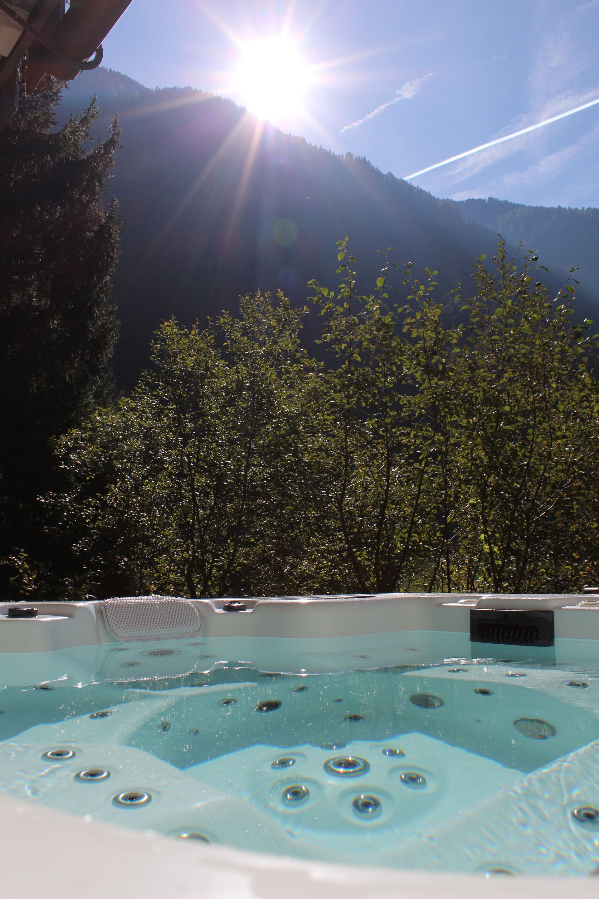 Ein strahlend sonniger Blick auf eine Berglandschaft über den Rand eines sprudelnden, hellblauen Whirlpools.