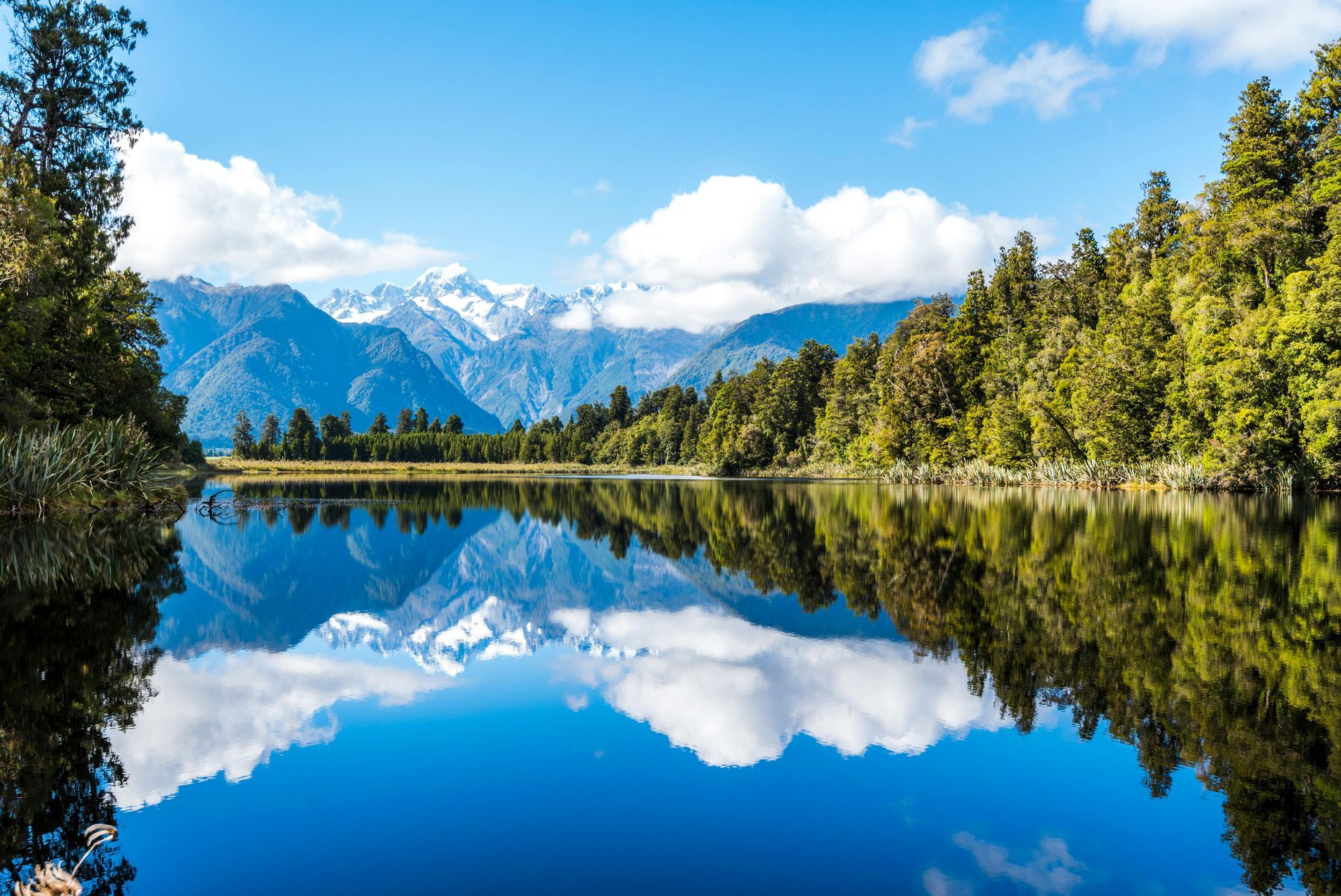 Schneebedeckte Berge und üppig grüne Bäume spiegeln sich perfekt im stillen, blauen Wasser des Lake Matheson in Neuseeland.