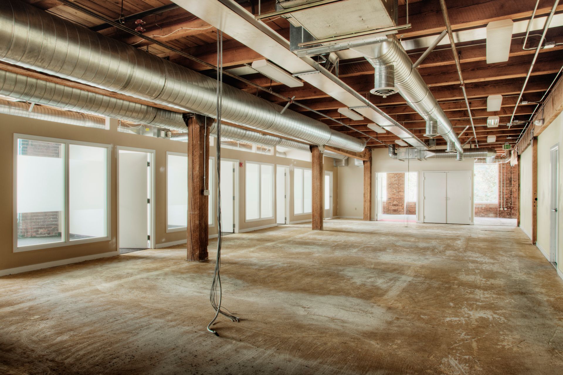 Empty unfinished office space with exposed beams, concrete floor, and large windows