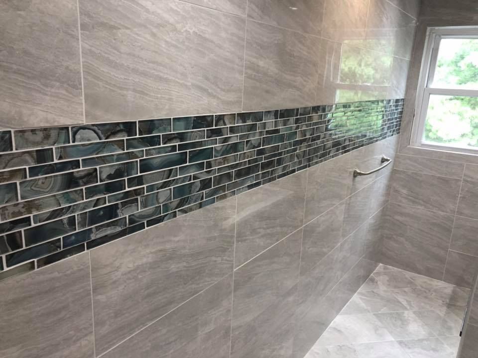 A bathroom with gray tiles and a window.