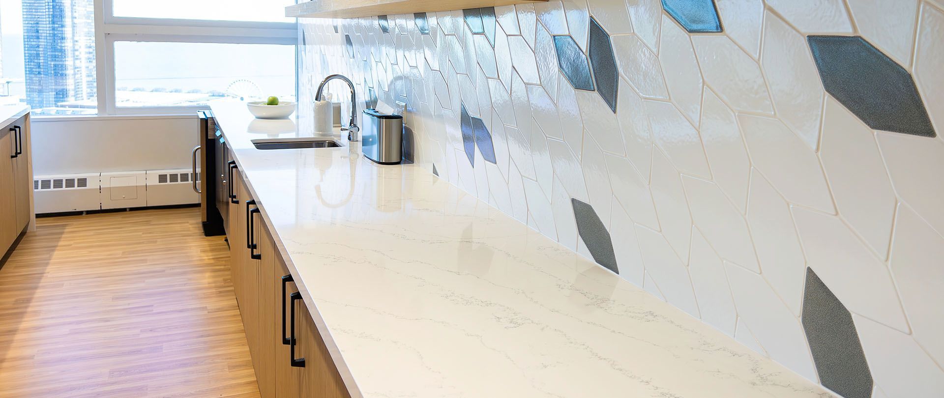 A kitchen with white countertops, leaf-patterned backsplash, and a window.