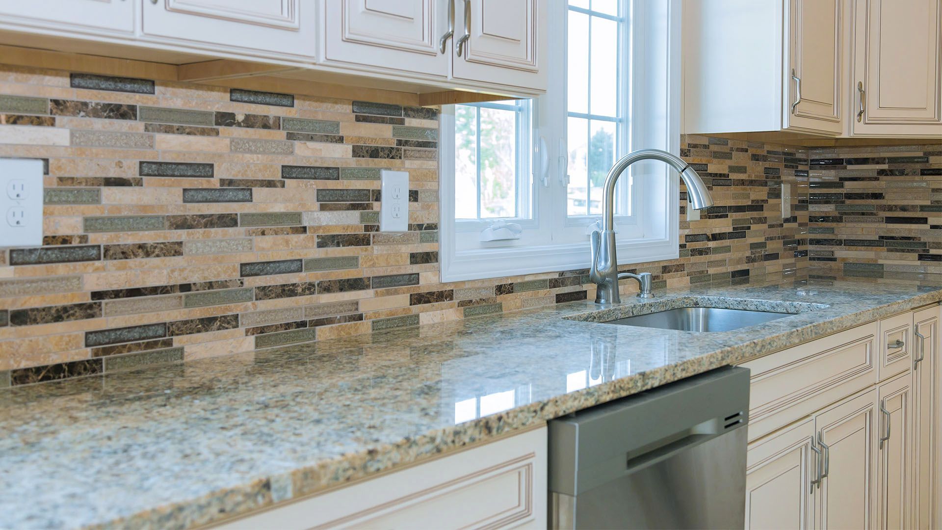 Kitchen with white cabinets, granite countertop, stainless steel sink and backsplash tile.