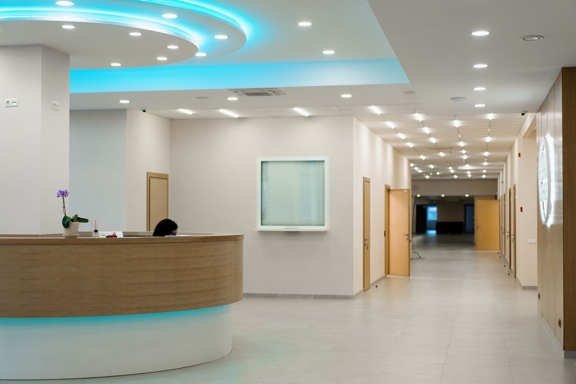 Reception area in a modern medical office with a wooden desk, white walls, and a long hallway under bright recessed lights.