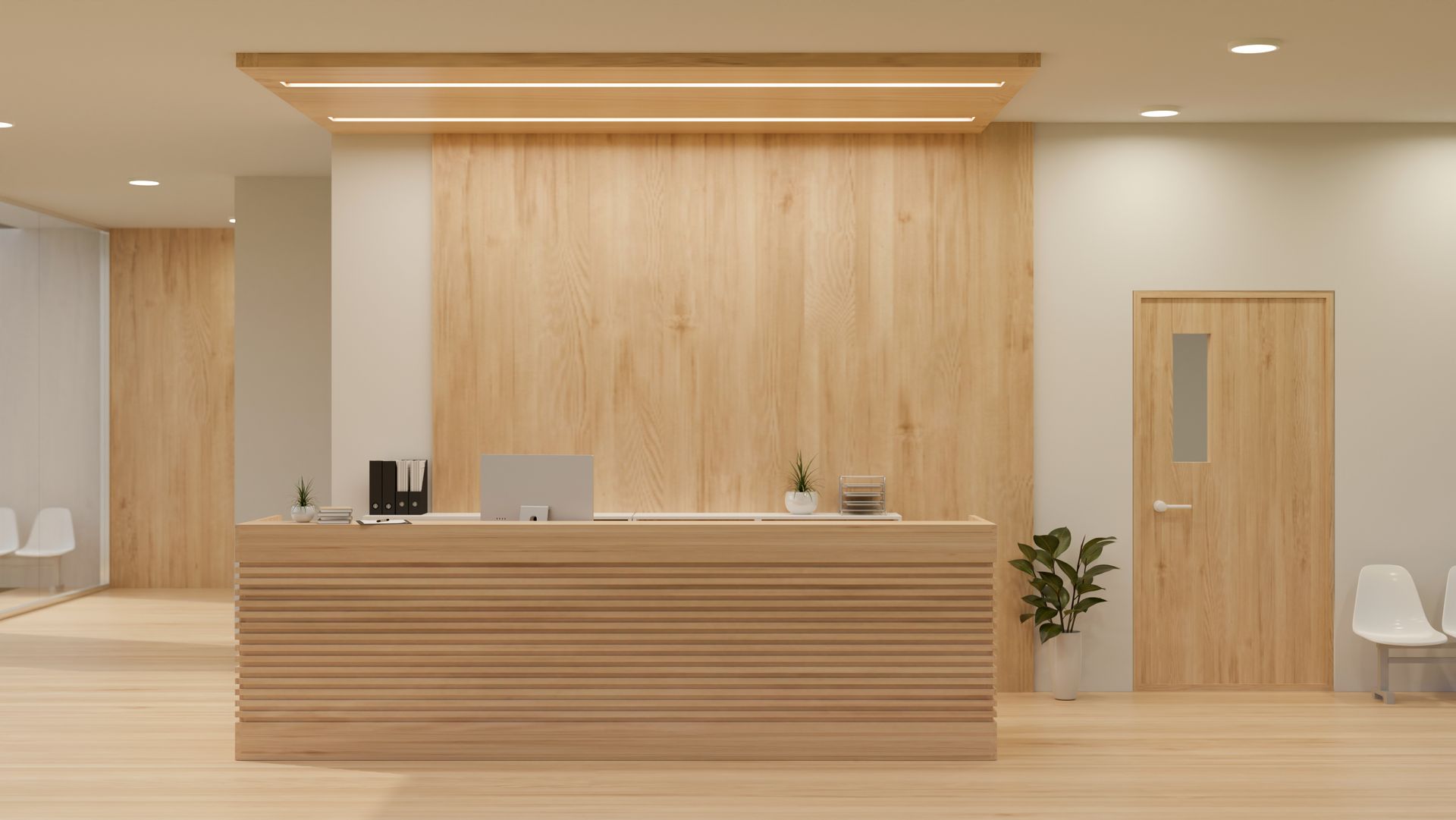Reception desk in a clinic, light wood paneling, computer, door, potted plant, waiting chairs.