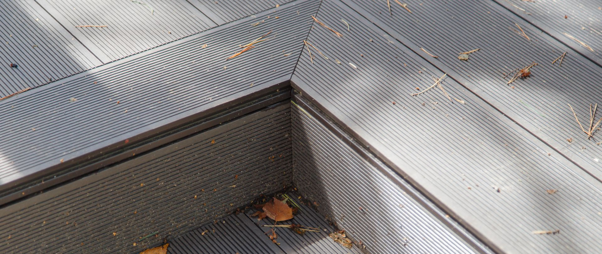 Close-up of a gray, grooved deck with a corner drain, scattered with leaves and debris.