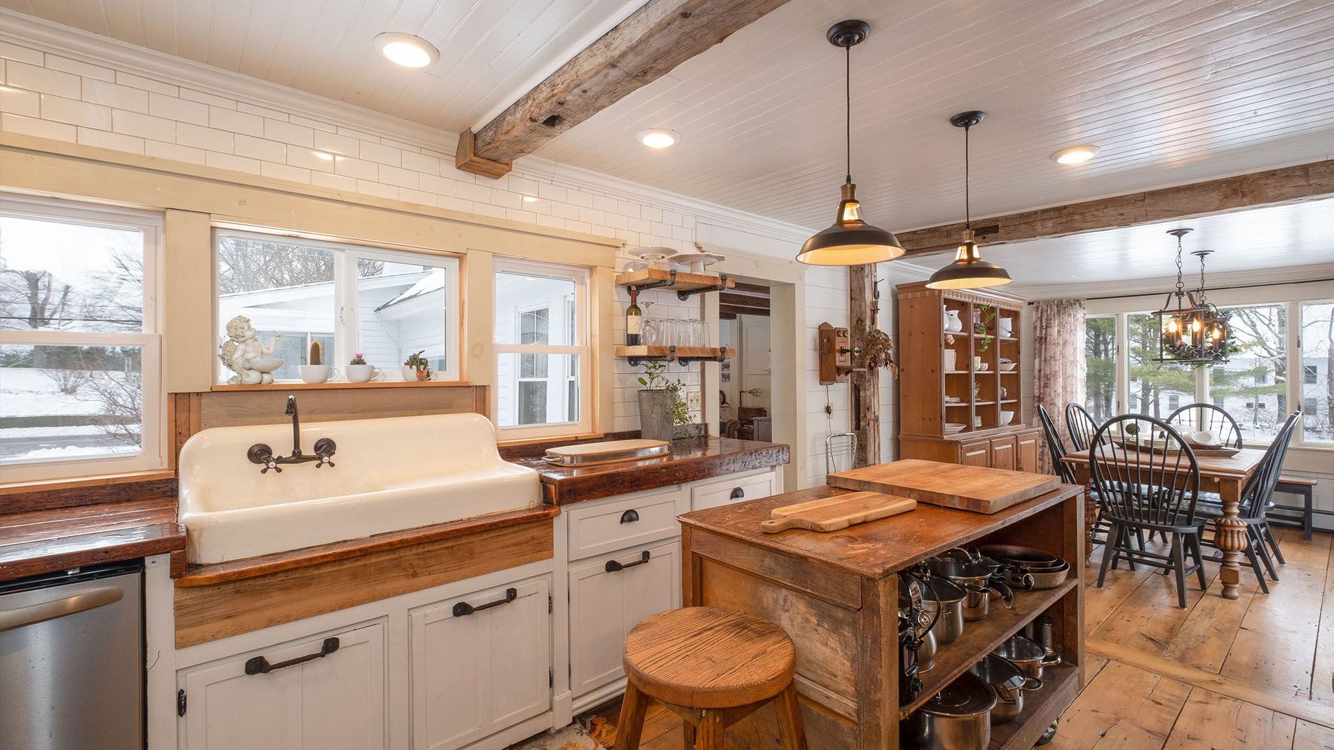 Rustic kitchen with white cabinets, wooden countertops, large sink, and dining area.