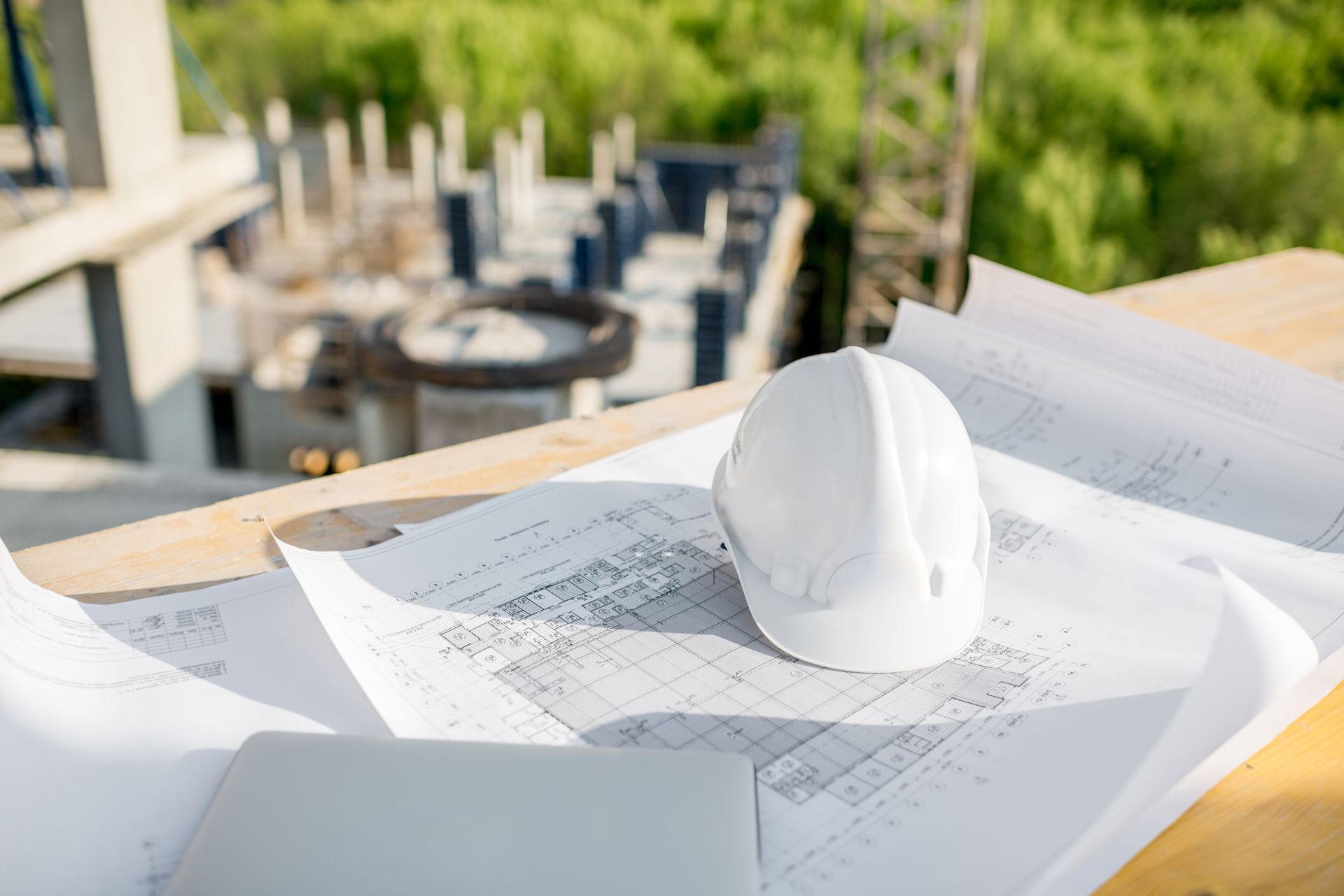 White hard hat on architectural blueprints at an outdoor construction site table.