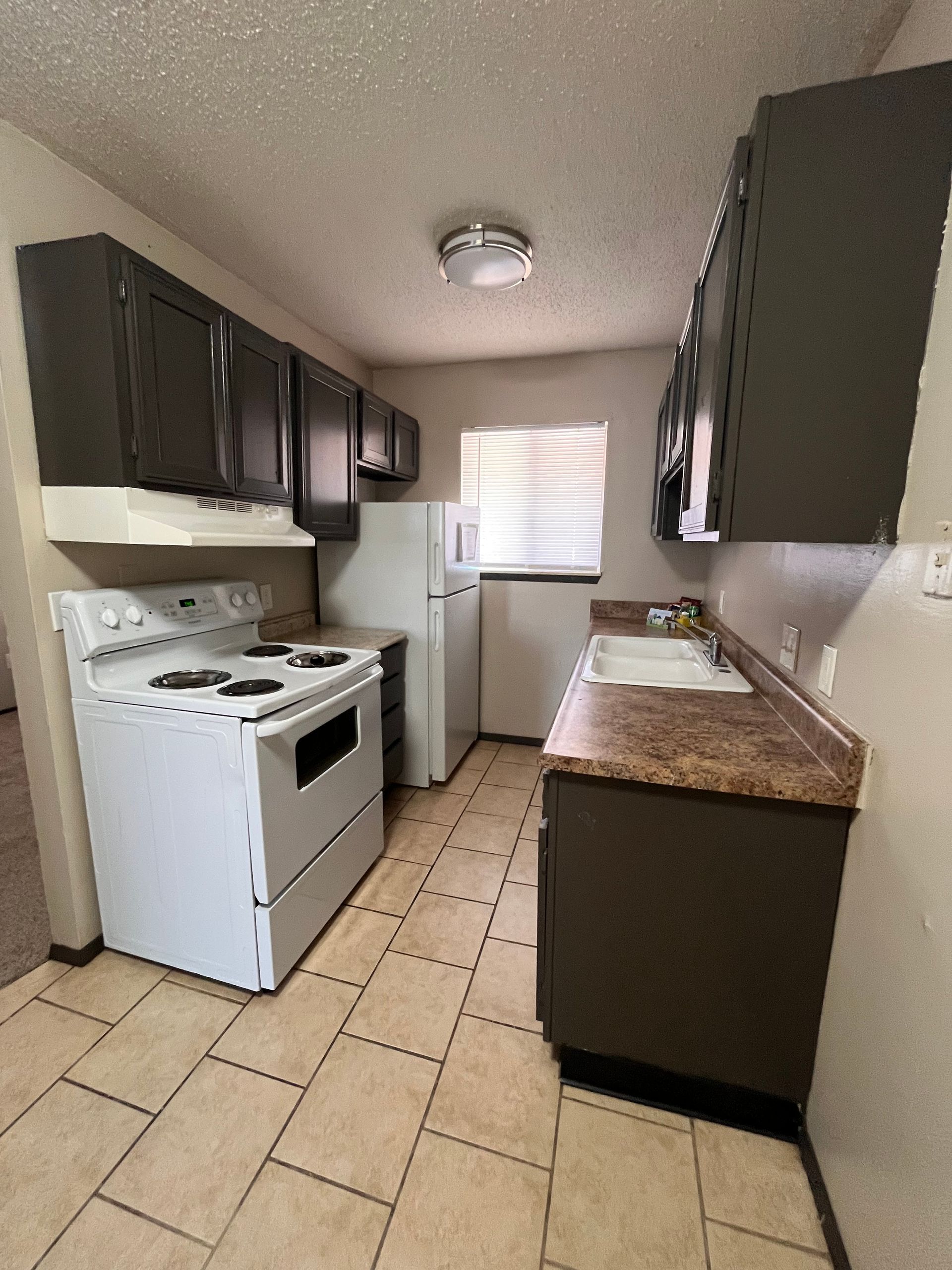 Small kitchen with white appliances, dark brown cabinets, and tan countertops and flooring.