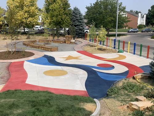 Colorful playground with painted designs, trees, and fence.