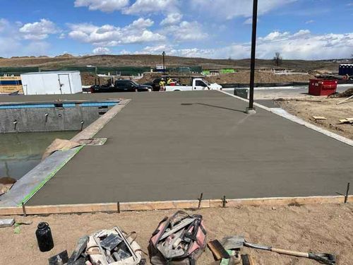 Freshly poured concrete patio beside a pool, construction site. Tools, white truck, blue sky with clouds.