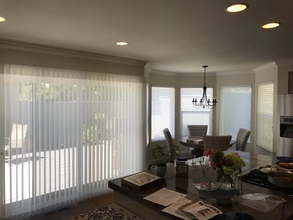 Bright interior kitchen with vertical blinds and dining area, natural light.