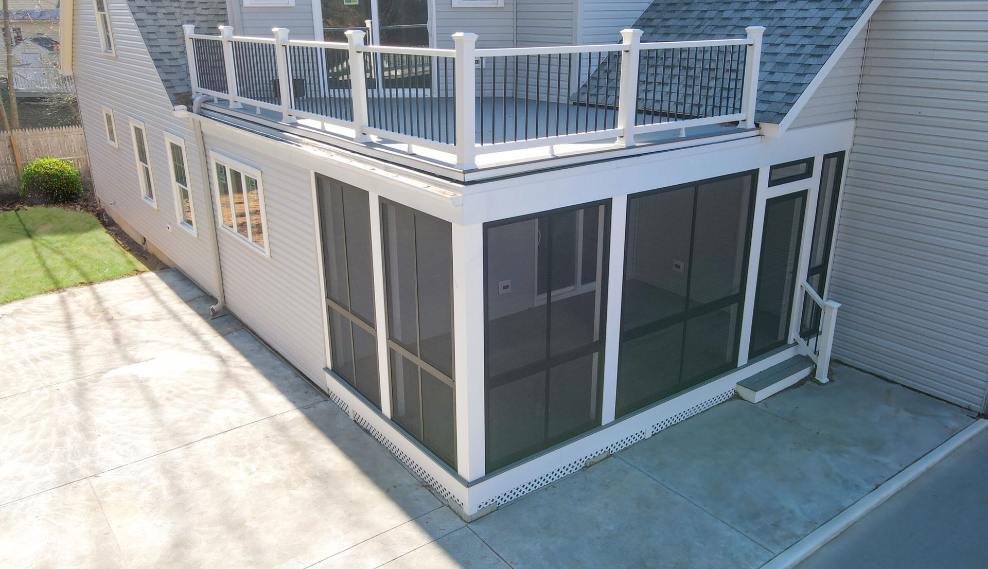 Exterior of a house with a screened porch and upper deck. White and gray building with a concrete patio.