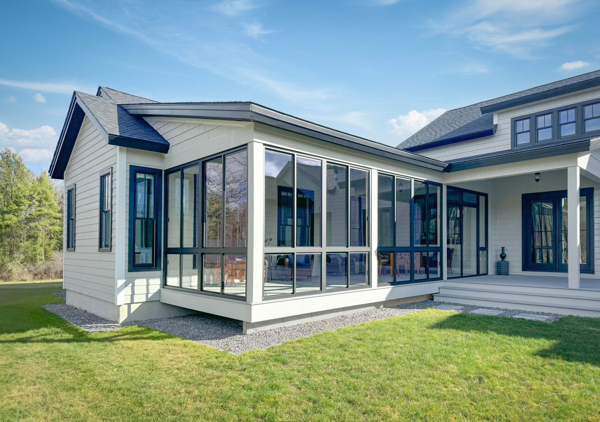 White house with glass-enclosed sunroom. Green lawn, blue sky. Modern architecture.