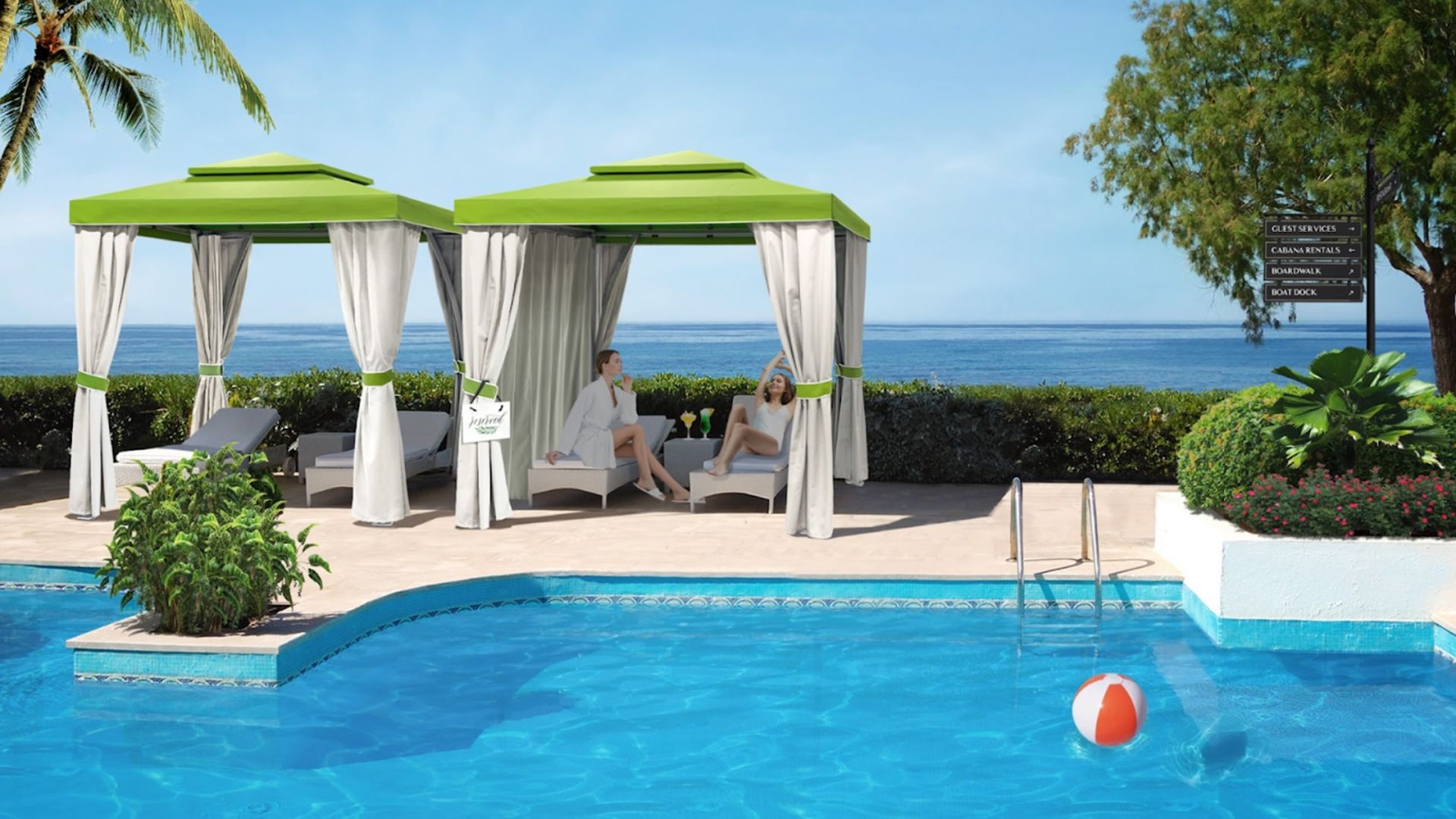 Two green-roofed cabanas with white curtains sit by a blue swimming pool with an ocean view in the background.