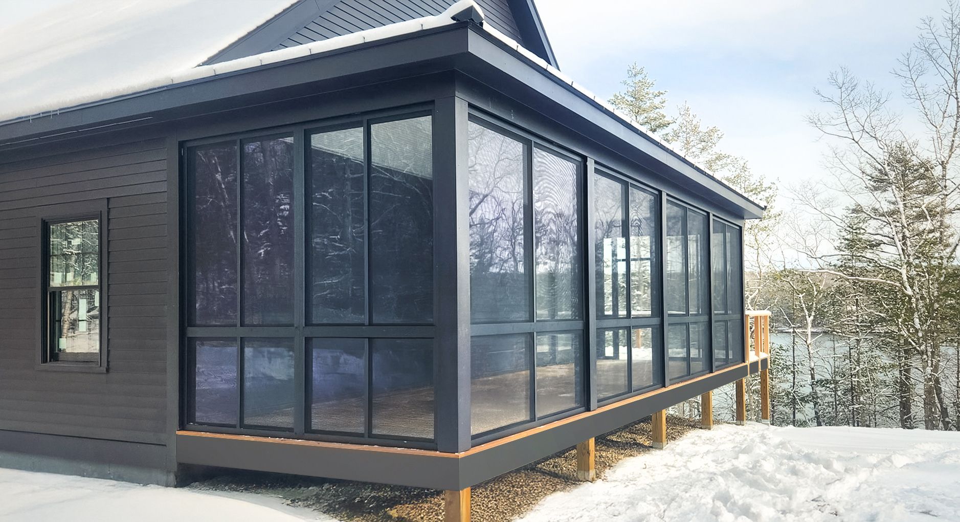 Dark gray sunroom with large windows, attached to a house, snowy landscape visible.