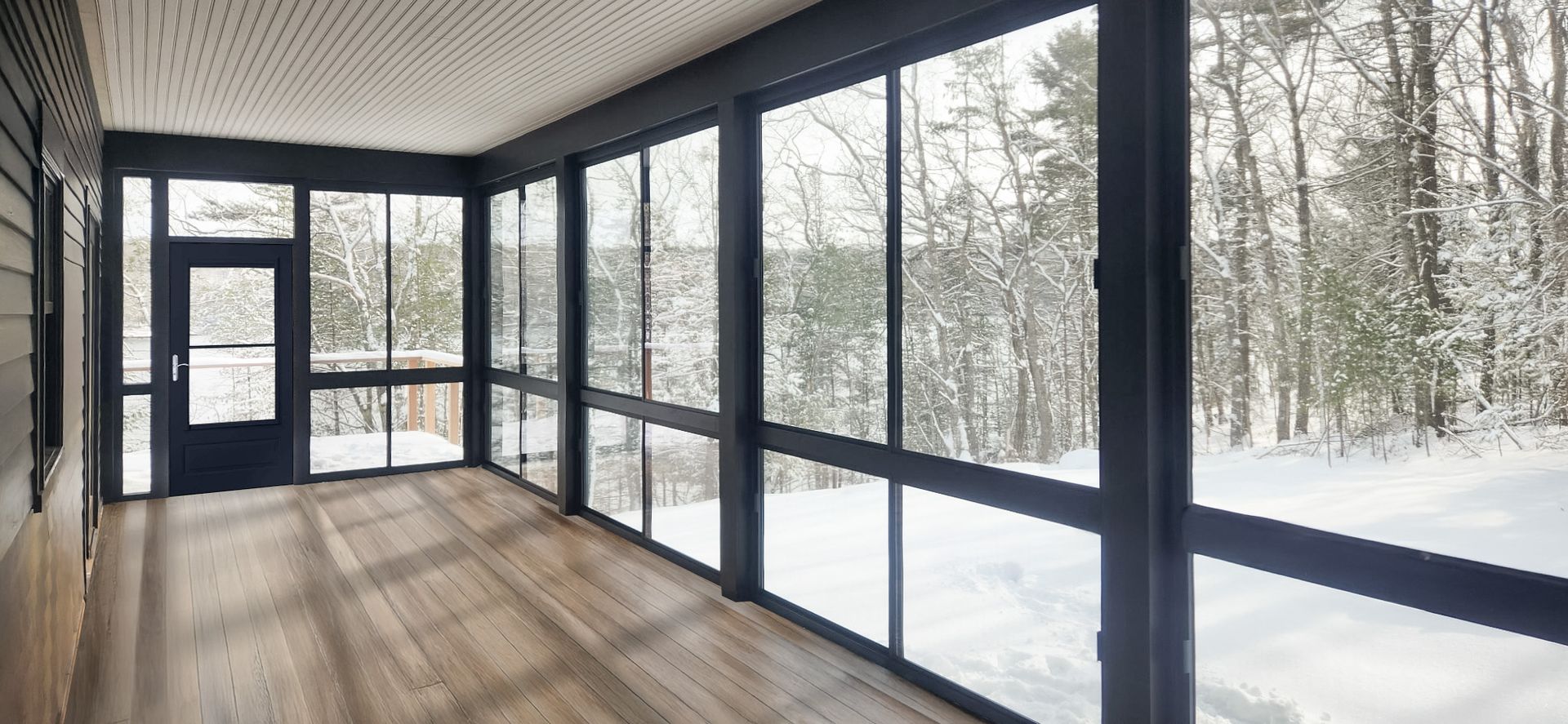 Sunroom with large windows overlooking a snowy forest.