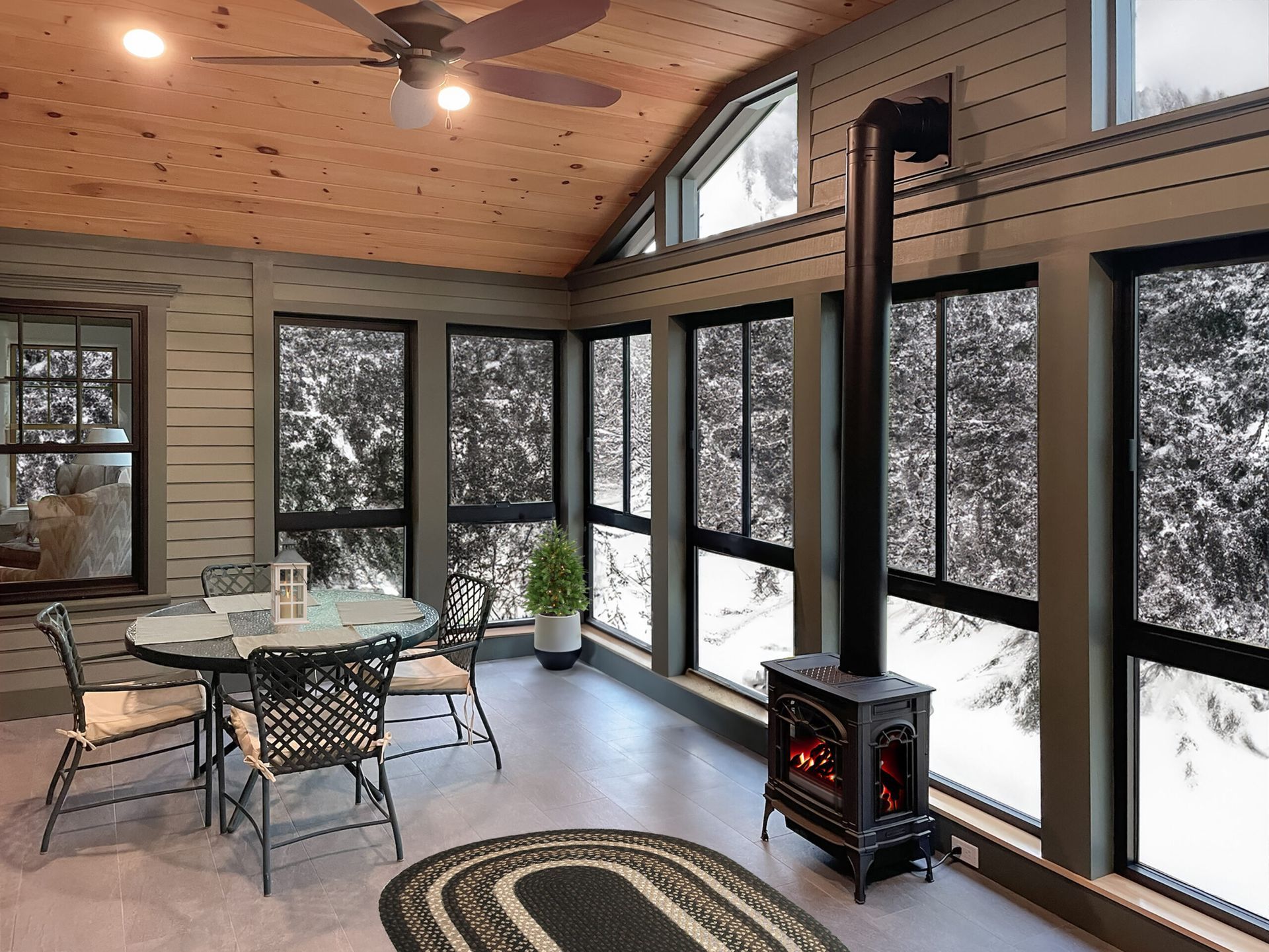 Sunroom with a fireplace, round table and chairs, and large windows with a snowy view.