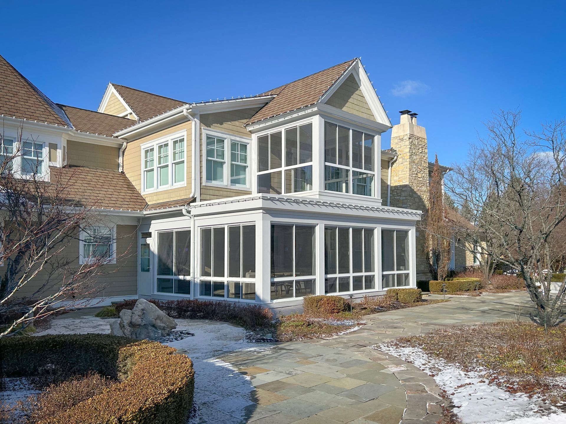Two-story beige house with screened-in porch and snow-covered walkway.
