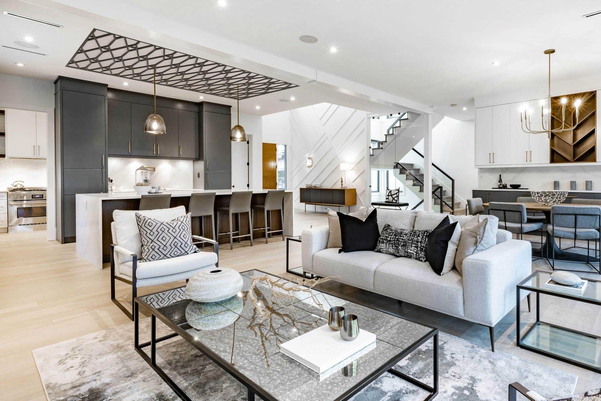 Modern open-concept living area with grey kitchen cabinets, a white sofa, and a glass coffee table in a bright room.