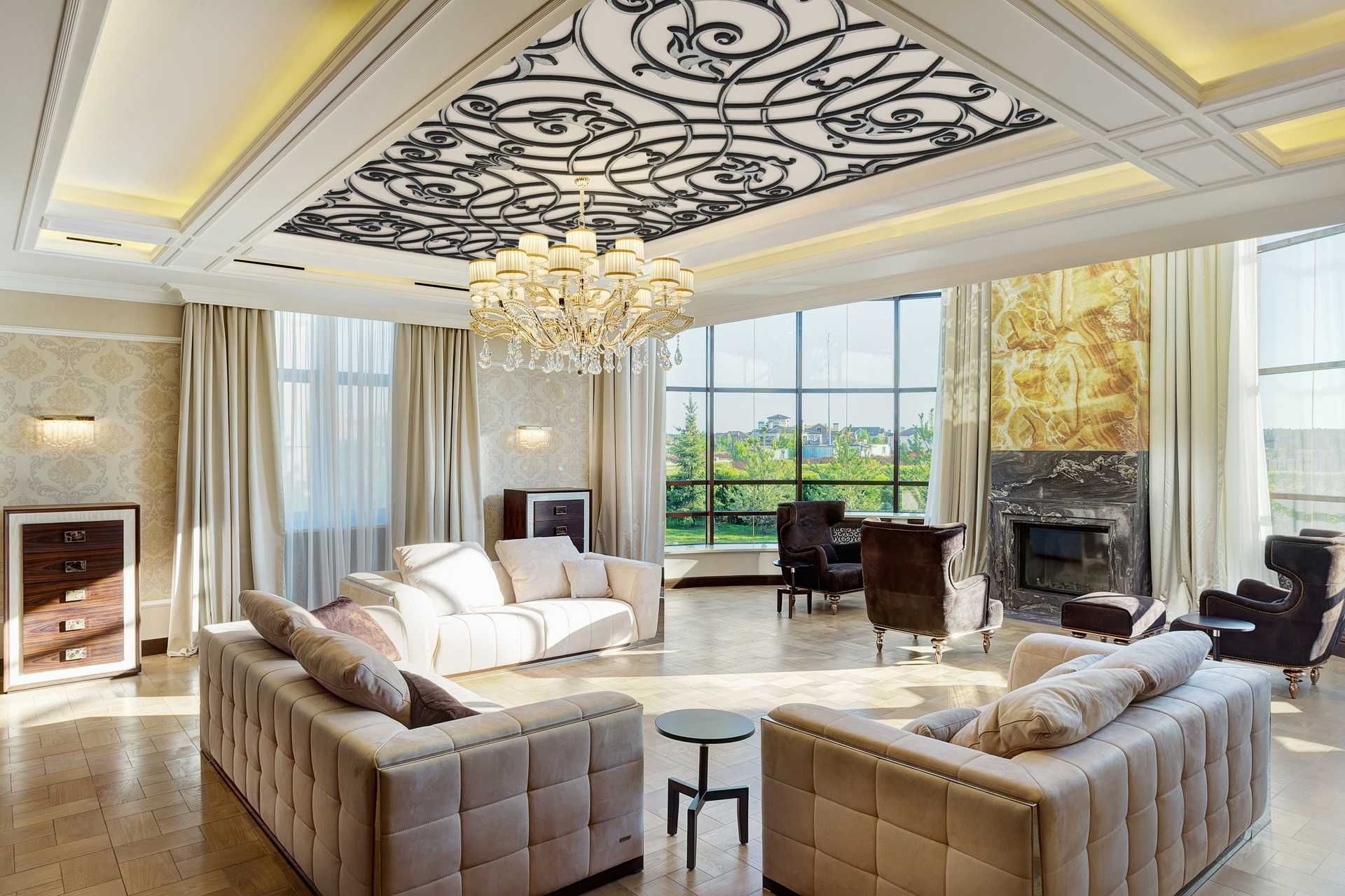 A luxurious, sunlit living room with cream tufted sofas, a central crystal chandelier, and a decorative ceiling panel.