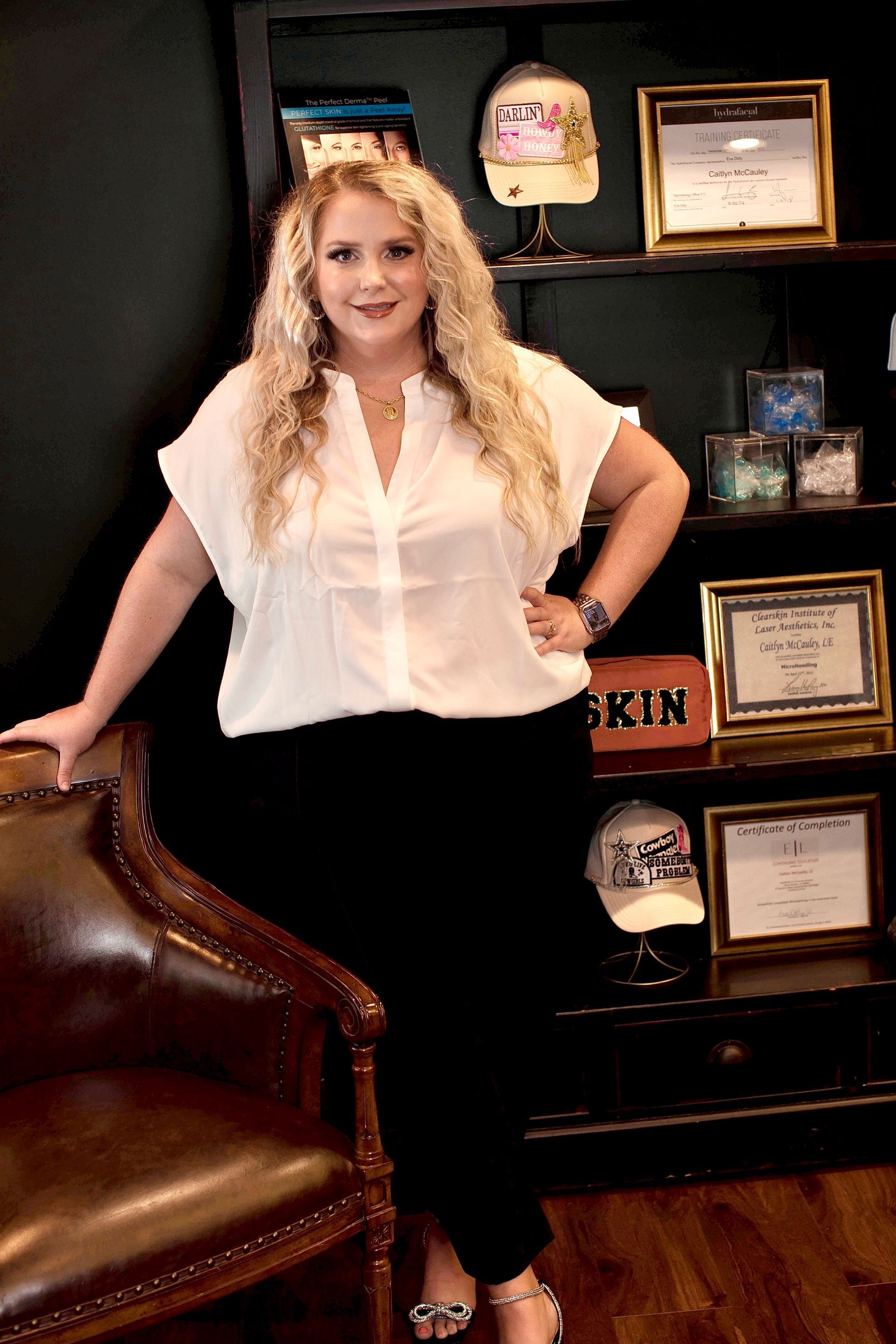 A woman is standing next to a chair in front of a bookshelf.
