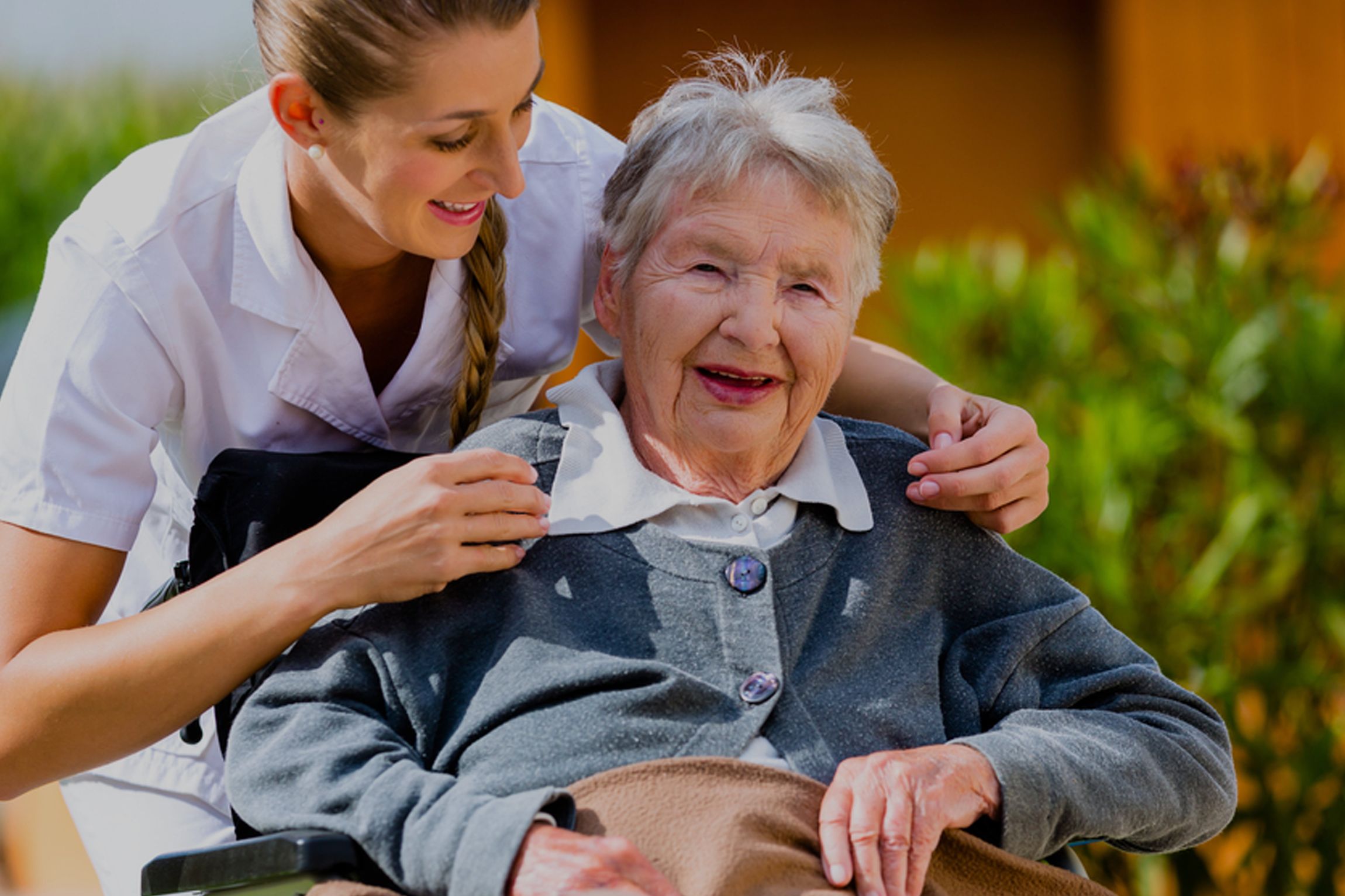 Dame im Rollstuhl bei der Seniorenbetreuung mit fürsorglicher Pflegerin