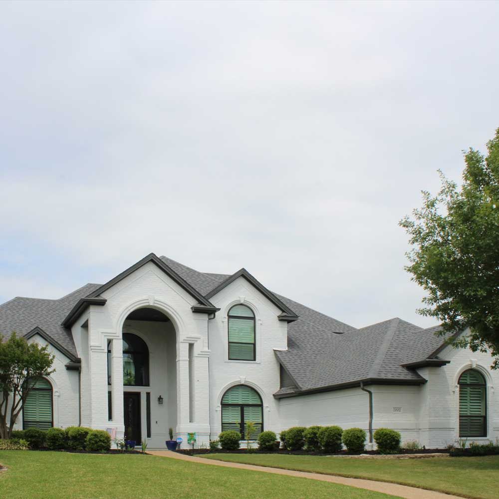 A large white house with a gray roof is sitting on top of a lush green lawn.