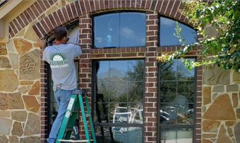 A man on a ladder is installing a window on a brick building.