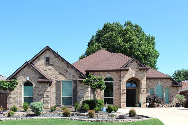 A large brick house with a brown roof, new window replacements and an entry door