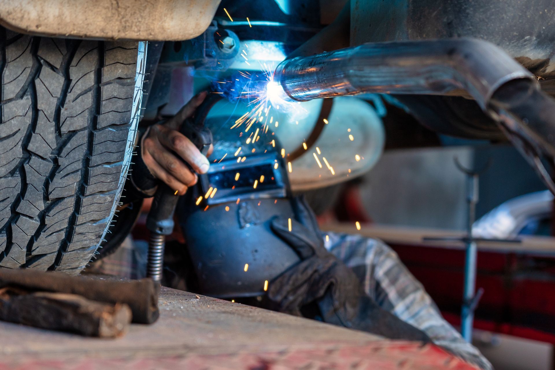 Welder welding a car exhaust pipe, sparks flying.