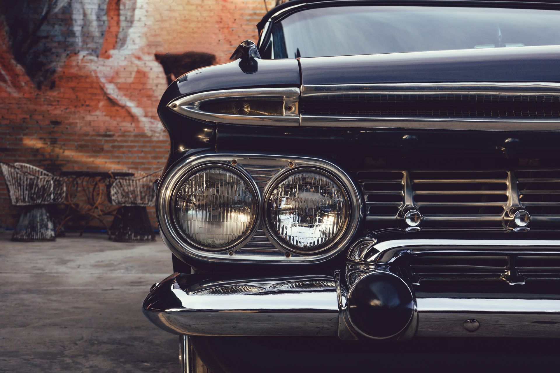 Classic black car's front with chrome accents, round headlights, and a mural in the background.