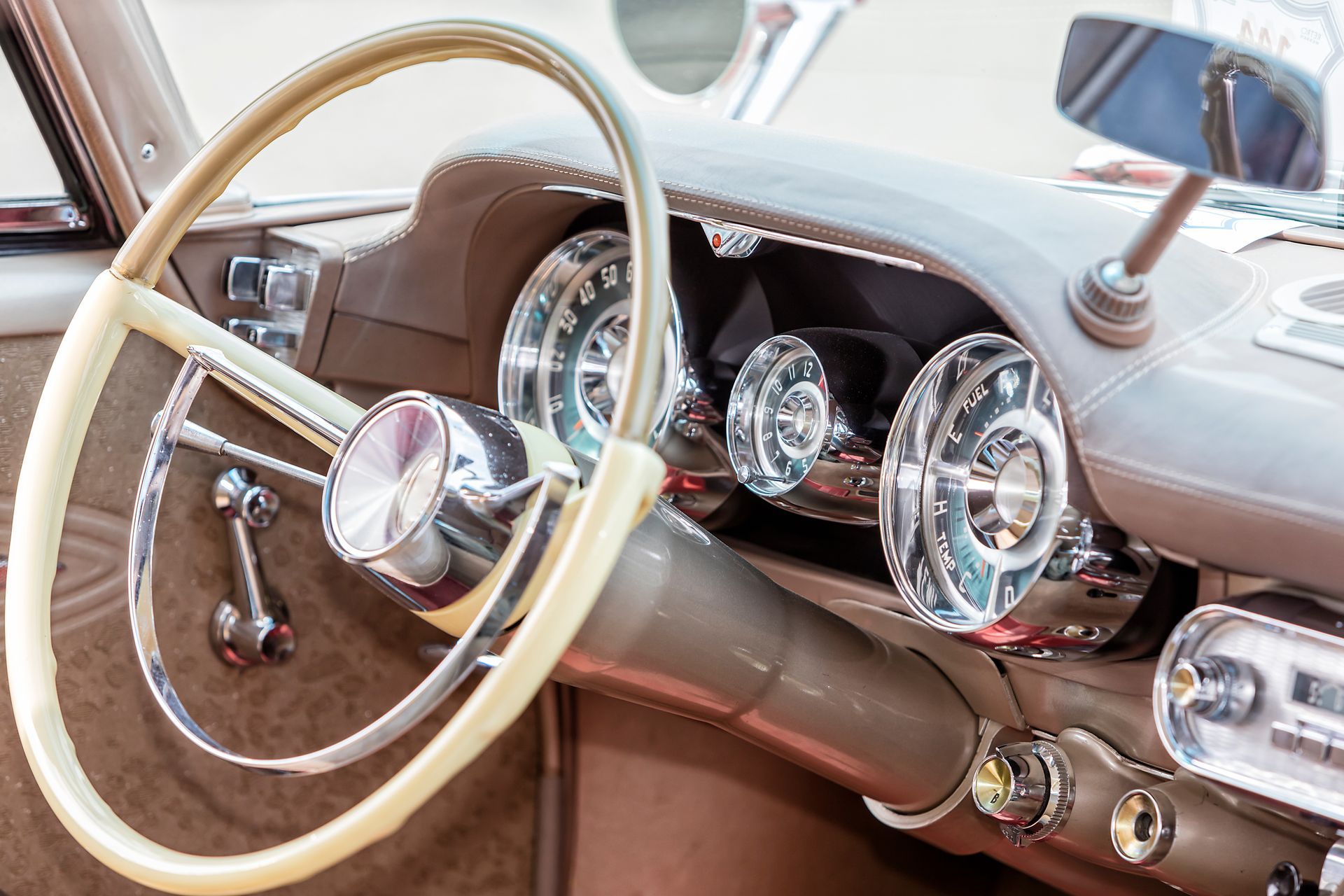 Cream-colored steering wheel and dashboard gauges in a vintage car. 