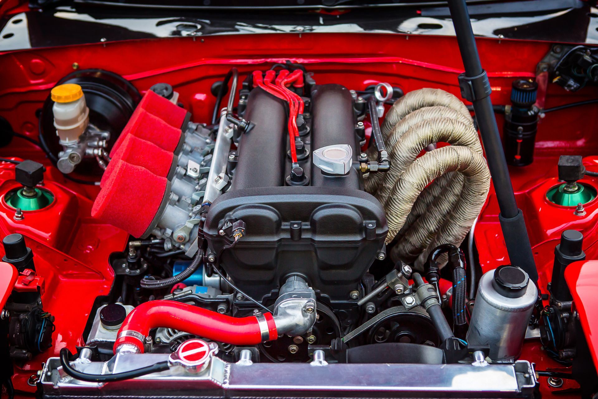 Red-painted car engine bay, showing engine with aftermarket parts and wrapped exhaust.