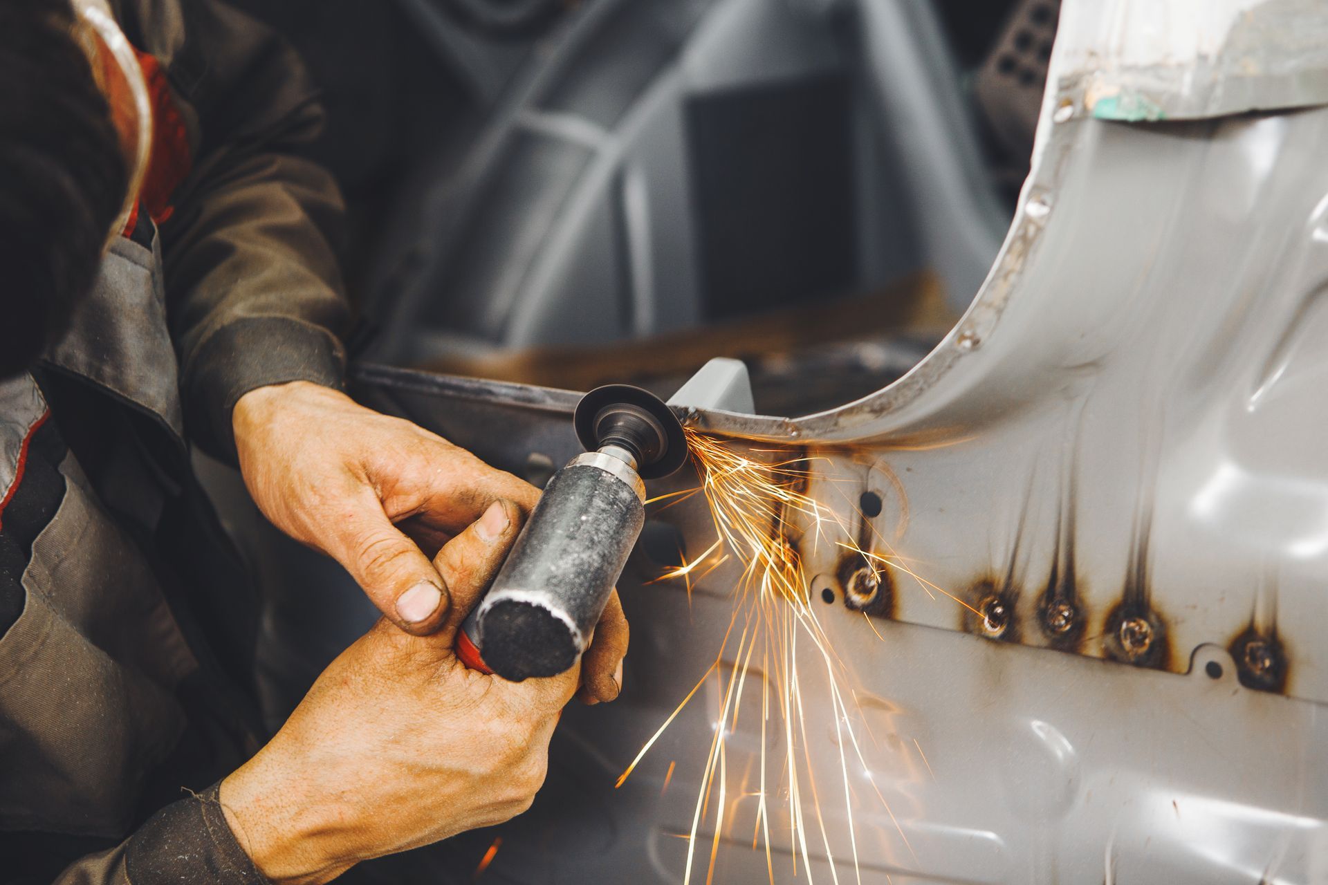 Person using a grinder, creating sparks, working on a car frame.