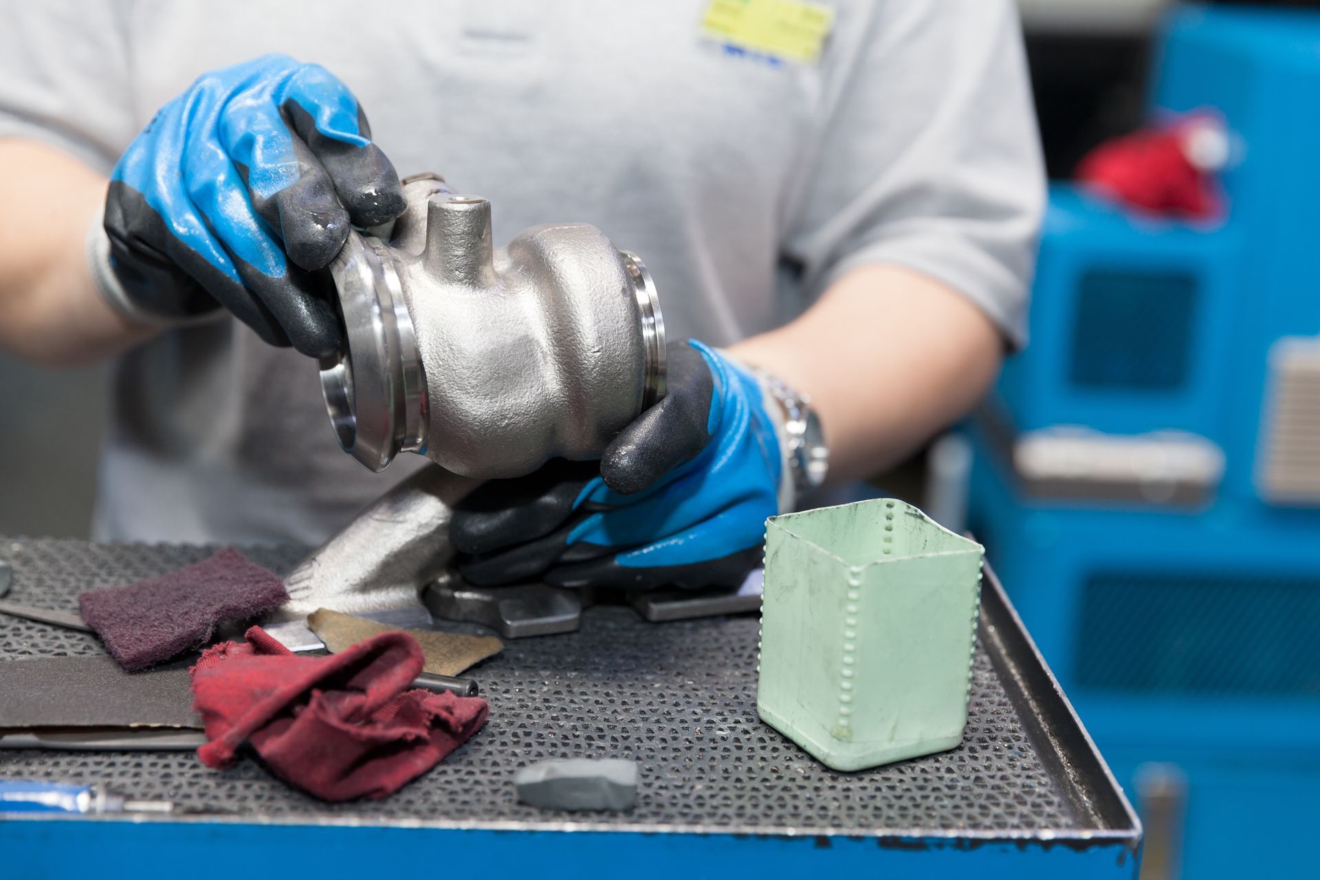 Person in blue gloves examining a metal part on a workbench.