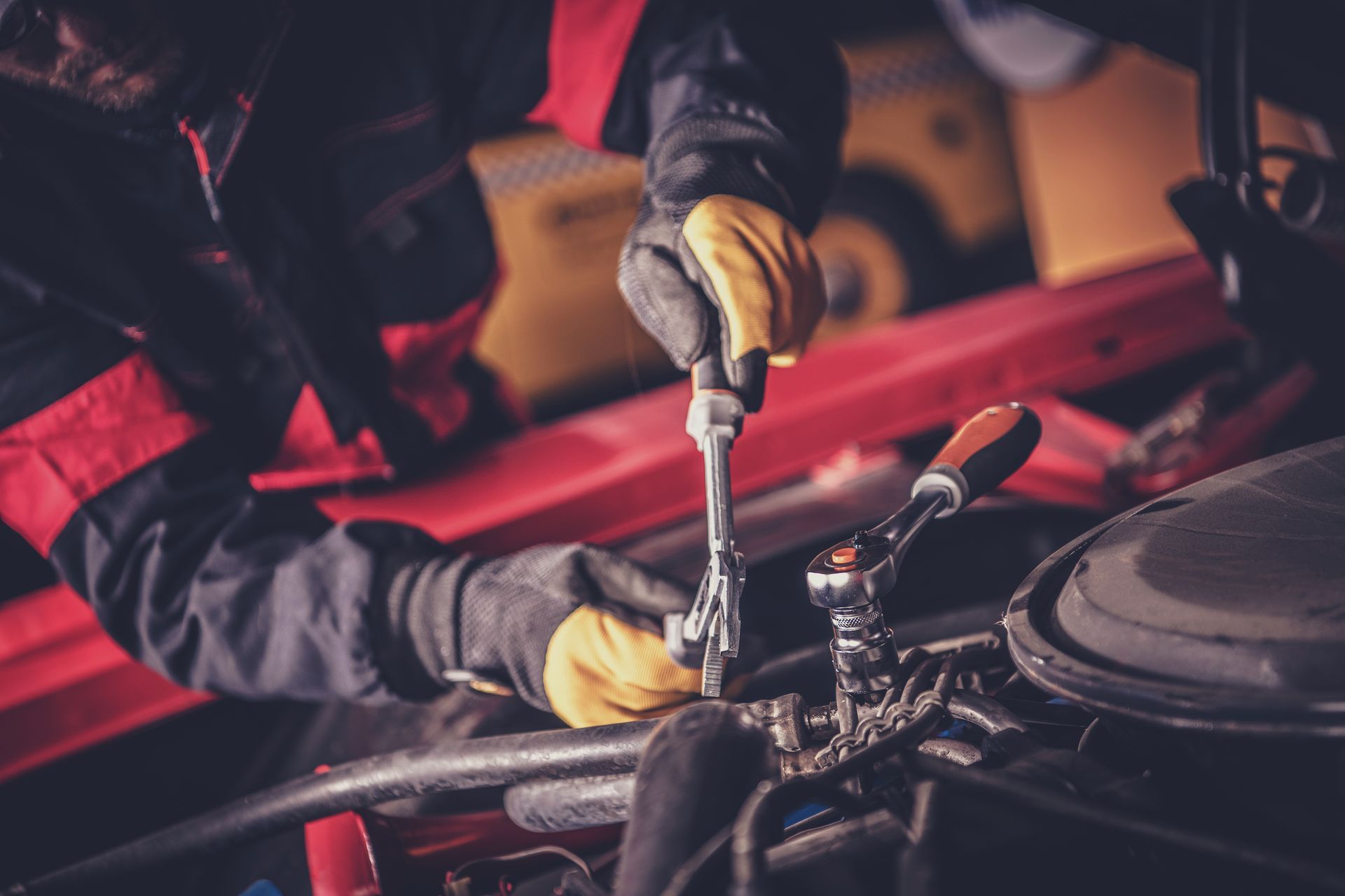 Mechanic in overalls uses a wrench on a car engine.