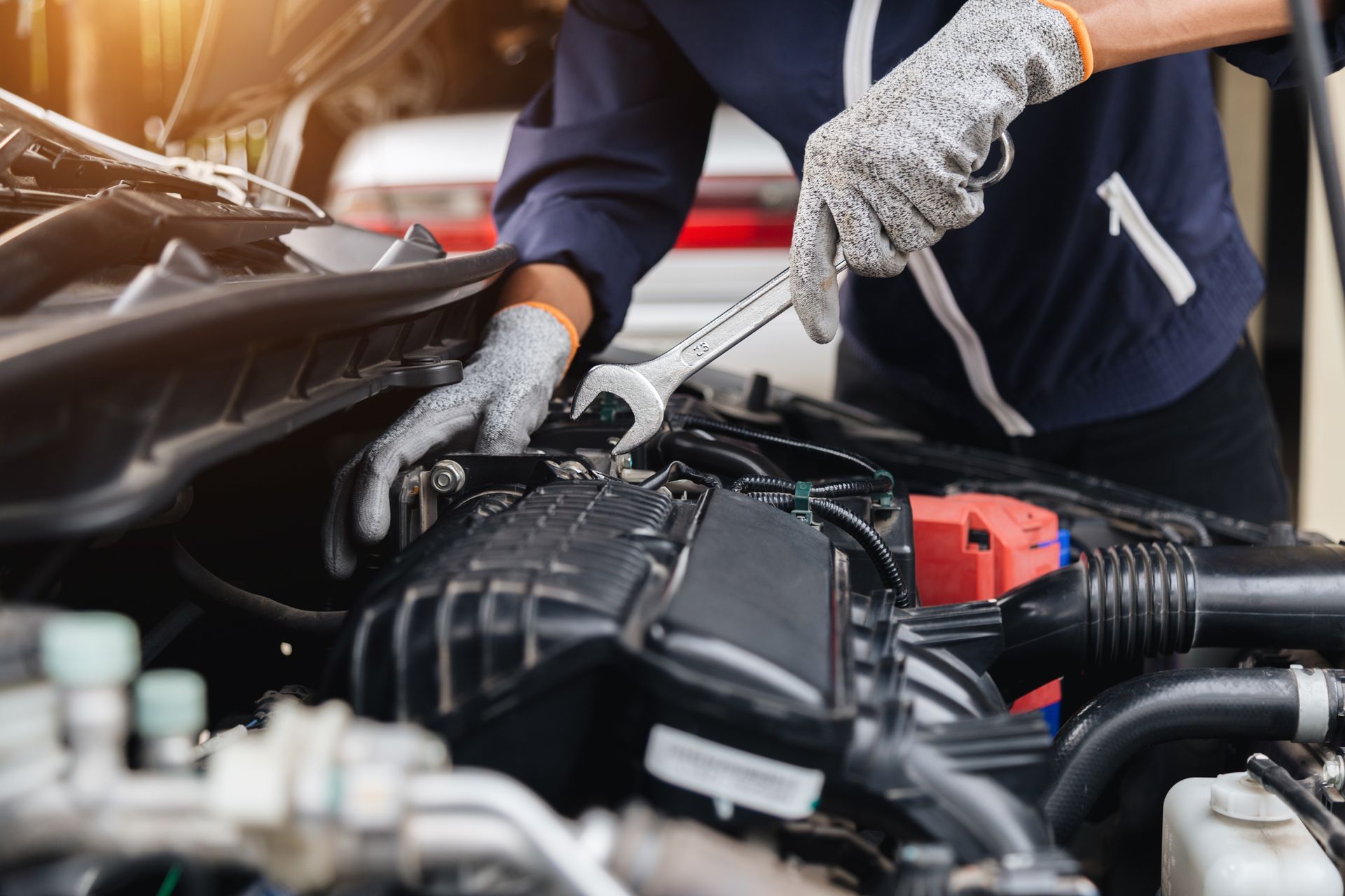 Mechanic working on a car engine, wearing gloves and using a wrench.